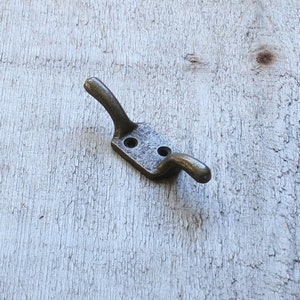 May include: A silver metal hook with two prongs. The hook is mounted on a light wood surface.