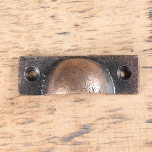 May include: A rectangular, antique copper-toned cabinet pull with a rounded top and two screw holes.
