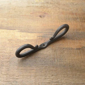 May include: Black metal double hook with a simple design. The hook is made of wrought iron and has a rustic finish.