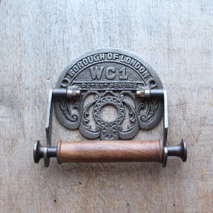 May include: A cast iron toilet roll holder with a decorative design featuring the words "Borough of London" and "WC1" with the words "Patent Pending" below. The holder has a wooden roller and brass accents.