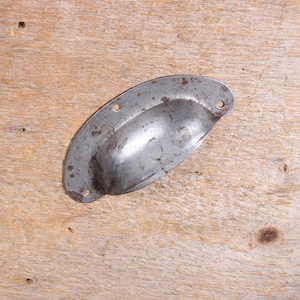 May include: A semi-circular metal cup pull handle featuring a weathered, grey finish with visible patches of brown rust. The hardware includes two small circular mounting holes on each side of the curved grip for attachment to furniture.