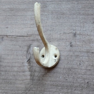 May include: A white metal hook with a curved design. The hook is mounted on a wooden surface.
