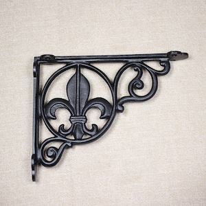 Peut inclure: Équerre d'étagère en fonte noire avec un motif de fleur de lys. Le support présente un emblème circulaire avec le symbole de la fleur de lys et des volutes décoratives. Conçu pour soutenir une étagère, il est adapté à la décoration intérieure.