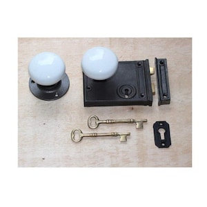 May include: An antique door hardware set featuring a black cast iron mortise lock, two white porcelain door knobs, a strike plate, and two brass keys. The set includes a keyhole cover.
