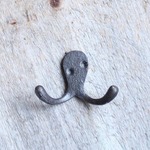 May include: A black metal double hook in the shape of an octopus. The hook is mounted on a light wood surface.