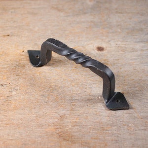 May include: Black metal door handle with a twisted design. The handle has a simple, elegant shape and is perfect for adding a touch of rustic charm to any door.