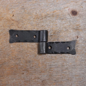 Peut inclure: Deux charnières noires avec une finition martelée. Chaque charnière présente un bord festonné décoratif et deux trous pré-percés pour le montage. Les charnières sont reliées par un joint cylindrique, permettant le mouvement. Idéal pour un style rustique ou vintage.
