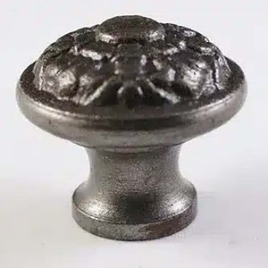 May include: A dark grey cabinet knob with a decorative floral design on the top. The knob has a rounded shape with a textured surface and a short, cylindrical base. Suitable for drawers and cabinets.