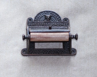May include: Antique cast iron toilet paper holder with a decorative design and the text "SANITARY PAPER BURYSTREET LONDON EC".