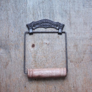 Peut inclure: Un porte-papier toilette de style vintage, avec une structure en métal foncé et un rouleau en bois. Le haut du support porte l'inscription en relief "BRITISH PAPER CO LONDON". Monté sur une surface en bois vieilli.