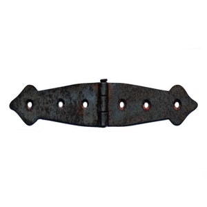 May include: A rusty black metal hinge with a decorative, pointed design on each end. The hinge is closed and ready to be attached to a door or other object.
