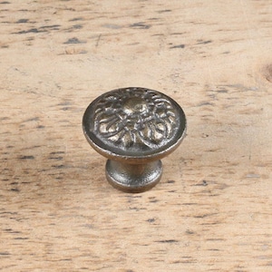 Op de afbeelding: Een kastknop van gietijzer met een decoratief bloemmotief. De knop is donkergrijs.