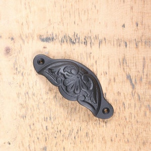 May include: Black cast iron drawer pull with a floral design. The pull is curved and has a traditional style.