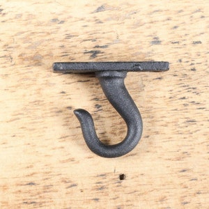 May include: Black metal hook with a square base. The hook is attached to a wooden surface.