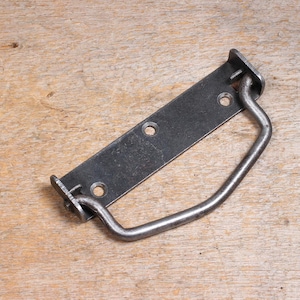 May include: A dark gray metal handle with a rectangular base and a curved handle. The base has three holes for mounting. The handle is made of a sturdy metal and is designed for use on a cabinet or drawer.