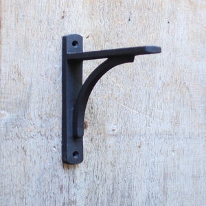 May include: Black metal shelf bracket with a curved design. The bracket is mounted to a wooden wall.