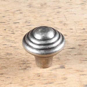 Peut inclure: Un bouton de porte en métal argenté avec un dessus arrondi et une série d'anneaux concentriques autour du dessus. Le bouton a une petite base ronde.