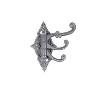 Könnte beinhalten: Ein silberner Wandhaken aus Metall mit dekorativem Design und drei Haken. Der Haken ist auf einem weißen Hintergrund montiert.