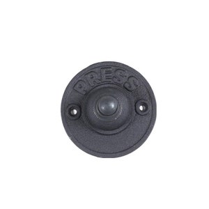 May include: A black metal doorbell button with the word "PRESS" embossed on the front. The button has a round, raised center with a small, round, silver button.