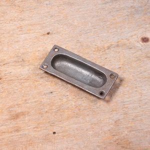 Peut inclure: Une poignée de tiroir rectangulaire en métal argenté avec une poignée ovale encastrée.