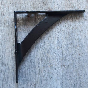 May include: A black metal shelf bracket with a curved support and a right-angle design. The bracket is painted black and has a simple, functional aesthetic. The bracket is designed to support a shelf.