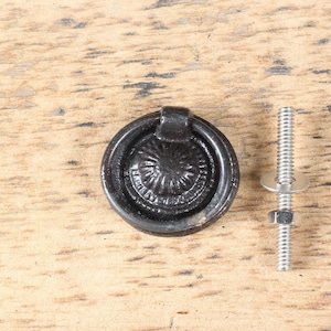 May include: Black metal cabinet knob with a ring pull and a decorative design. The knob comes with a screw for installation.