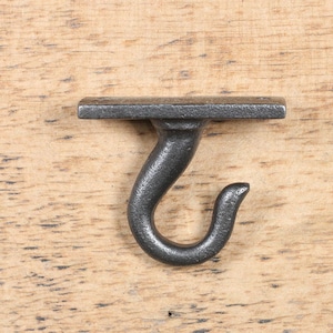 Peut inclure: Un crochet en métal noir avec une base plate. Le crochet est fixé à une surface en bois.