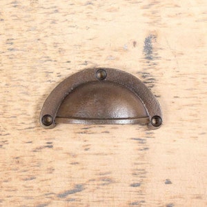 Pode incluir: Uma puxador de gaveta de metal marrom com uma forma arredondada e abobadada. A puxador tem uma superfície ligeiramente texturizada e quatro pequenos parafusos.