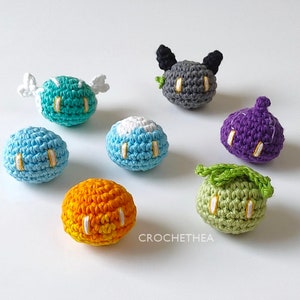 Puede incluir: Una colección de siete peluches de crochet en varios colores, incluyendo azul, verde, morado, naranja y gris. Cada peluche tiene un diseño único y ojos bordados.