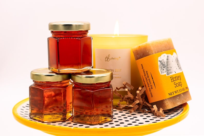 May include: Three small glass jars filled with honey, a yellow candle with the word "thriving" on the front, and a bar of honey soap with the text "Honey Soap, Net Wt 1.5 oz" on the label. The items are arranged on a yellow and black polka dot plate.