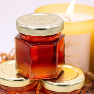 May include: Three small glass jars with gold lids filled with honey. The jars are stacked on top of each other. The jars are in focus, and the background is blurred.