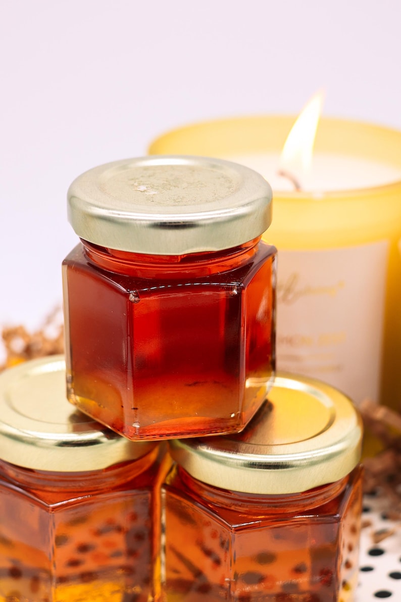 May include: Three small glass jars with gold lids filled with honey. The jars are stacked on top of each other. The jars are in focus, and the background is blurred.