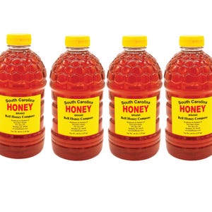 May include: Four clear plastic bottles of South Carolina Honey, a brand of Bell Honey Company. Each bottle is filled with a thick, amber-colored honey and has a yellow label with the brand name and information about the honey.