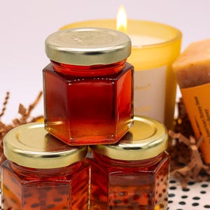 May include: Three small glass jars filled with honey, stacked on top of each other. The jars have gold lids and are on a black and white polka dot surface.