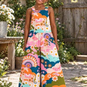May include: A sleeveless jumpsuit featuring a vibrant, multi-colored pattern of horses, flowers, butterflies, and mushrooms against a background of teal, pink, and orange clouds. The garment has wide legs and a square neckline with thick shoulder straps.
