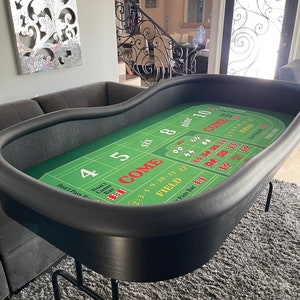 May include: A green felt craps table with black felt edges and a black felt border. The table has a variety of betting areas, including "Come", "Don't Pass", "Pass Line", and "Field".