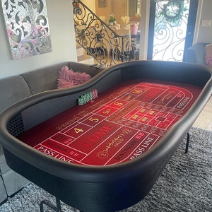 May include: A red felt craps table with black trim and a black base. The table has a layout for a craps game with numbers 2, 3, 4, 5, 6, 8, 9, 10, and 11, as well as the words "Come", "Don't Pass Bar", and "Pass Line".