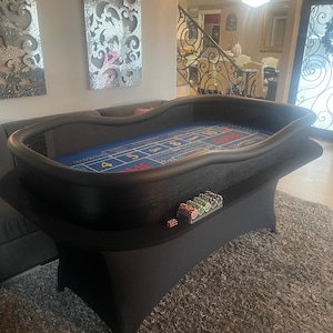 May include: Black felt-covered casino table with a blue felt playing surface and a roulette wheel layout. The table has a black felt skirt and a stack of poker chips on the side.