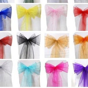 May include: Assortment of chair sashes in various colors, including blue, yellow, pink, red, black, gold, orange, light blue, turquoise, and purple. The sashes are made of sheer fabric and are tied into bows.
