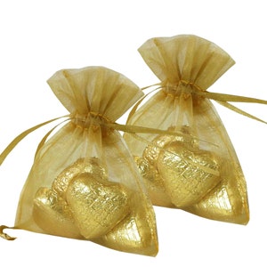 May include: Two gold organza bags filled with gold foil-wrapped heart-shaped chocolates. The bags have gold ribbon ties.