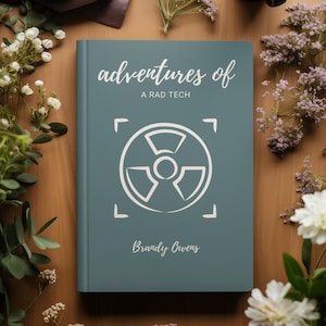 Op de afbeelding: Een blauwgroen boek met de titel "adventures of A RAD TECH", een wit stralingssymbool en de naam van de auteur, Brandy Owens. Het boek is omgeven door witte en paarse bloemen op een houten oppervlak.
