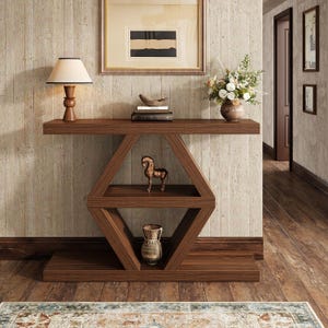 May include: A dark wood console table featuring a geometric diamond-shaped frame with two interior shelves. The table holds a lamp, books, a decorative bowl, a vase of flowers, a small bronze horse figurine, and a ceramic vase on the lower shelf.
