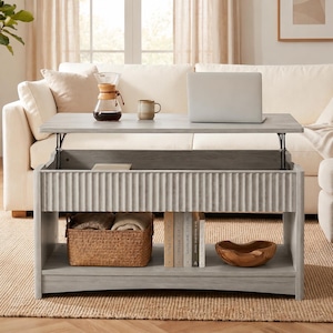 May include: A gray lift-top coffee table with a ribbed front panel and lower shelf. A woven basket, wooden bowl, and books are on the lower shelf. A laptop, coffee maker, and mug sit on the tabletop. The table is in front of a white sofa.