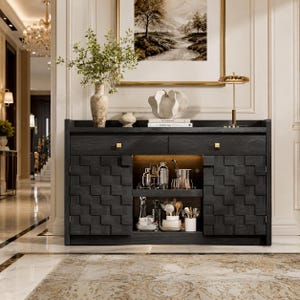 May include: A dark gray wooden sideboard with a geometric pattern on the doors. The sideboard has gold-colored hardware and an open shelf with barware. A painting and decorative items are on top.