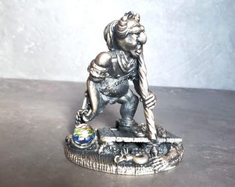 May include: A silver figurine of a goblin-like creature holding a staff. The figurine is standing on a base with a small, colorful glass orb and other decorative elements.