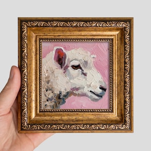 Könnte beinhalten: Ein Ölgemälde eines weißen Schafskopfes im Profil vor einem strukturierten rosa Hintergrund, gemalt mit dicken Impasto-Pinselstrichen. Das Kunstwerk ist in einem verzierten, antiken Goldrahmen mit einem geprägten Blattmuster gefasst.