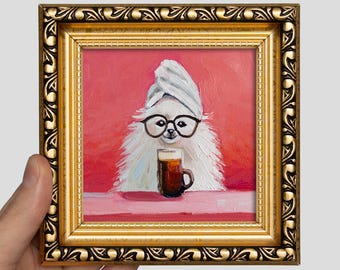 May include: An oil painting in a decorative gold frame depicting a fluffy white dog wearing a towel on its head and black-rimmed glasses, holding a dark brown mug of coffee against a solid pink background with a pink surface in the foreground.
