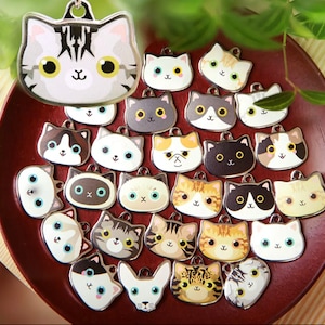 May include: A collection of silver cat charm pendants with various cat designs, including tabby, calico, and white cats. The charms feature different colored eyes and expressions.