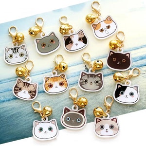 May include: A set of 12 cat charm keychains with gold bells. Each charm features a different cat breed with a unique expression. The charms are made of white plastic with colorful details.
