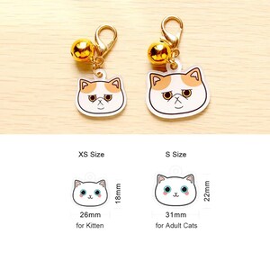 May include: Two cat-shaped cat collar charms with gold bells. The smaller charm is 26 mm wide and 18 mm tall, labeled "XS Size for Kitten". The larger charm is 31 mm wide and 22 mm tall, labeled "S Size for Adult Cats".